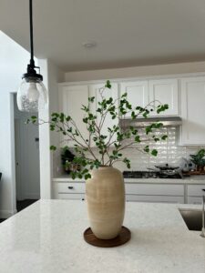 A meticulously cleaned modern kitchen with a white marble countertop, where a ceramic vase with fresh greenery exemplifies the attention to detail of our house cleaning service.
